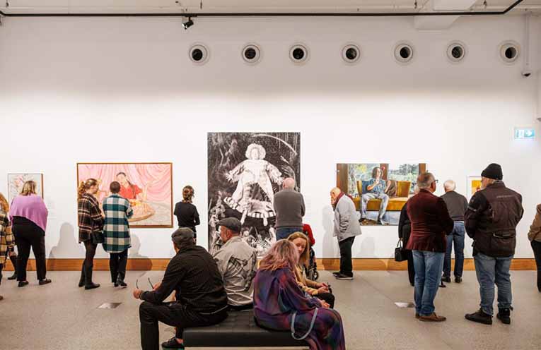 Visitors in the Archibald Prize 2025 exhibition at Yarrila Arts and Museum featuring (left-right) Fiona Lowry Ken Done, Angela Brennan Bridget in my painting.